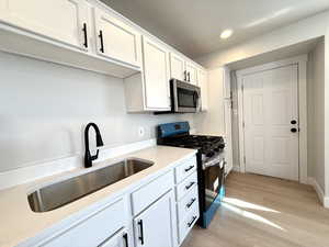 Kitchen with white cabinetry, sink, light wood-type flooring, and appliances with stainless steel finishes