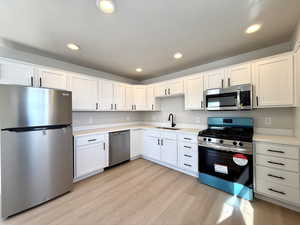 Kitchen with white cabinetry, sink, stainless steel appliances, and light hardwood / wood-style floors