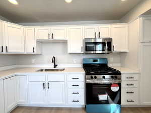 Kitchen with white cabinetry, appliances with stainless steel finishes, sink, and light hardwood / wood-style floors