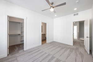 Unfurnished bedroom with ensuite bathroom, a walk in closet, light colored carpet, ceiling fan, and a closet