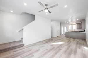 Unfurnished living room featuring ceiling fan with notable chandelier and light wood-type flooring