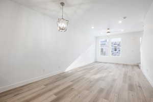 Spare room with ceiling fan with notable chandelier and light hardwood / wood-style flooring