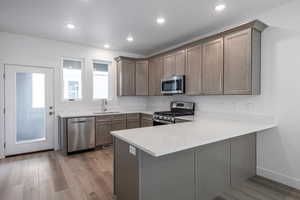 Kitchen with sink, light hardwood / wood-style flooring, kitchen peninsula, and appliances with stainless steel finishes