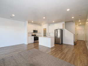 Kitchen with dark wood-type flooring, stainless steel appliances, a kitchen island with sink, and white cabinets