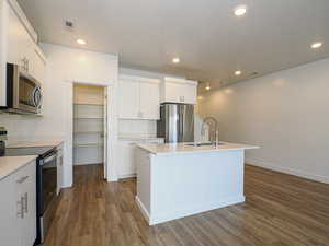 Kitchen featuring sink, dark wood-type flooring, appliances with stainless steel finishes, an island with sink, and white cabinets