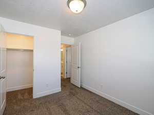 Unfurnished bedroom featuring a closet, a walk in closet, a textured ceiling, and dark colored carpet