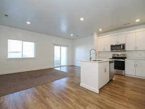 Kitchen featuring sink, an island with sink, stainless steel appliances, light hardwood / wood-style floors, and white cabinets