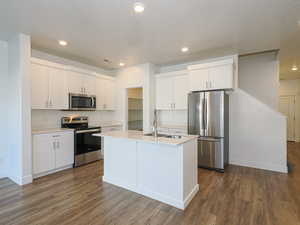 Kitchen with sink, dark wood-type flooring, white cabinetry, stainless steel appliances, and an island with sink