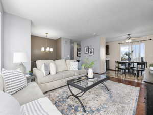 Living room with dark hardwood / wood-style floors and ceiling fan with notable chandelier. View of dining room and slider to wraparound deck