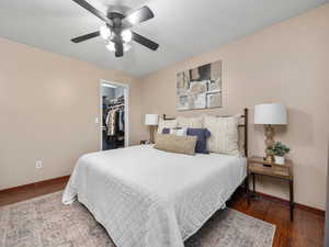 Primary bedroom with ceiling fan, a walk in closet, dark hardwood / wood-style flooring