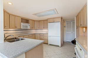 Kitchen with white appliances, light brown cabinetry, sink, and backsplash