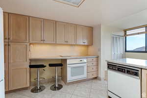 Kitchen with a breakfast bar area, light stone counters, light tile patterned floors, light brown cabinets, and white appliances