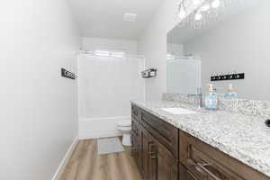 Full bathroom with vanity, shower / tub combo, hardwood / wood-style flooring, and toilet