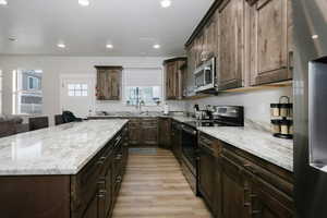 Kitchen featuring stainless steel appliances, dark brown cabinets, light stone counters, and light hardwood / wood-style floors