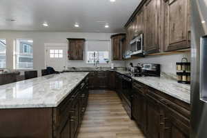 Kitchen with stainless steel appliances, light stone countertops, dark brown cabinetry, and light hardwood / wood-style flooring