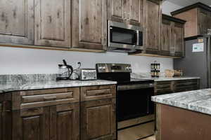 Kitchen with light stone countertops, appliances with stainless steel finishes, and dark brown cabinetry