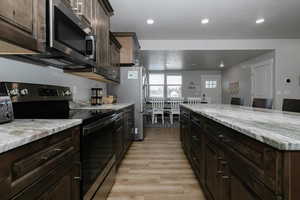 Kitchen featuring light stone counters, stainless steel appliances, dark brown cabinets, and light hardwood / wood-style flooring