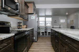 Kitchen with light stone countertops, dark brown cabinets, stainless steel appliances, and light hardwood / wood-style floors