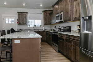 Kitchen with a kitchen island, a breakfast bar area, light hardwood / wood-style floors, stainless steel appliances, and light stone countertops