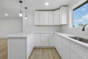 Kitchen featuring white cabinetry, decorative light fixtures, kitchen peninsula, and sink