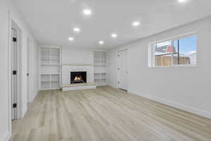 Unfurnished living room featuring built in shelves, a fireplace, and light hardwood / wood-style floors