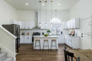 Kitchen featuring sink, hanging light fixtures, stainless steel appliances, white cabinets, and wall chimney exhaust hood