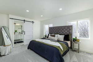 Bedroom featuring light colored carpet, a barn door, and ensuite bathroom