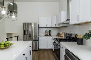 Kitchen with pendant lighting, appliances with stainless steel finishes, light stone countertops, and white cabinets