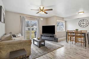 Living room with ceiling fan, a textured ceiling, and light wood-type flooring