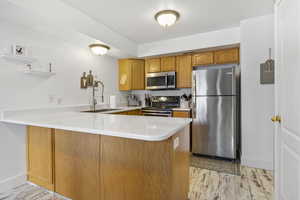 Kitchen with sink, light hardwood / wood-style floors, kitchen peninsula, stainless steel appliances, and a textured ceiling