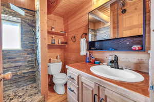 Bathroom featuring wooden walls, a shower, vanity, toilet, and wooden ceiling