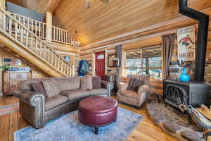 Living room featuring hardwood / wood-style floors, wood ceiling, log walls, and a wood stove