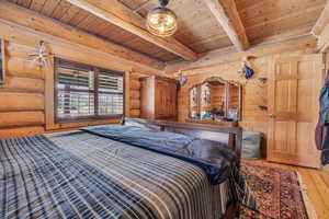 Bedroom featuring hardwood / wood-style flooring, rustic walls, wooden ceiling, and beamed ceiling