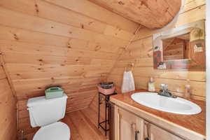 Bathroom with lofted ceiling, toilet, wood-type flooring, and wood walls