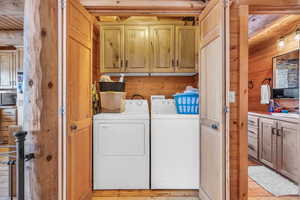 Laundry room featuring cabinets, washer and dryer, wooden walls, and light wood-type flooring