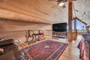 Living room with vaulted ceiling with beams, wooden walls, wood ceiling, and light hardwood / wood-style flooring