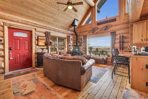 Living room featuring high vaulted ceiling, light wood-type flooring, wooden ceiling, a wood stove, and ceiling fan