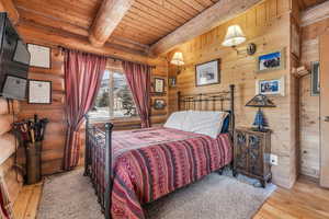 Bedroom with wood ceiling, beam ceiling, light hardwood / wood-style floors, and log walls