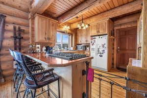 Kitchen featuring light hardwood / wood-style flooring, a breakfast bar, appliances with stainless steel finishes, hanging light fixtures, and kitchen peninsula