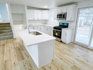 Kitchen featuring stainless steel appliances, a kitchen island with sink, sink, and white cabinets