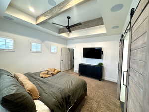 Bedroom with light colored carpet, ceiling fan, a tray ceiling, a barn door, and beam ceiling