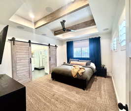 Bedroom featuring ensuite bath, a tray ceiling, beamed ceiling, ceiling fan, and a barn door