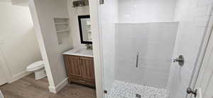 Bathroom with hardwood / wood-style floors, built in features, a shower with shower door, vanity, and toilet