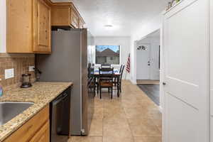 Kitchen with light tile patterned flooring, a textured ceiling, black dishwasher, light stone countertops, and backsplash