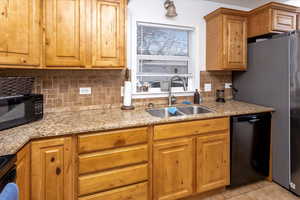 Kitchen with sink, light tile patterned floors, black appliances, and light stone countertops