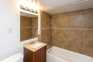 Full bathroom with tiled shower / bath, vanity, a textured ceiling, and toilet