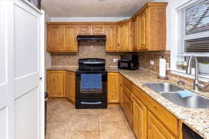 Kitchen with light tile patterned flooring, sink, light stone counters, and black appliances