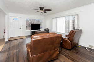 Living room with ceiling fan, a textured ceiling, and dark hardwood / wood-style flooring