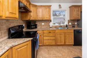 Kitchen featuring sink, light tile patterned floors, black appliances, light stone countertops, and decorative backsplash