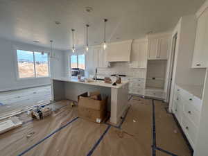 Kitchen featuring custom range hood, backsplash, white cabinetry, light countertops, and a textured ceiling